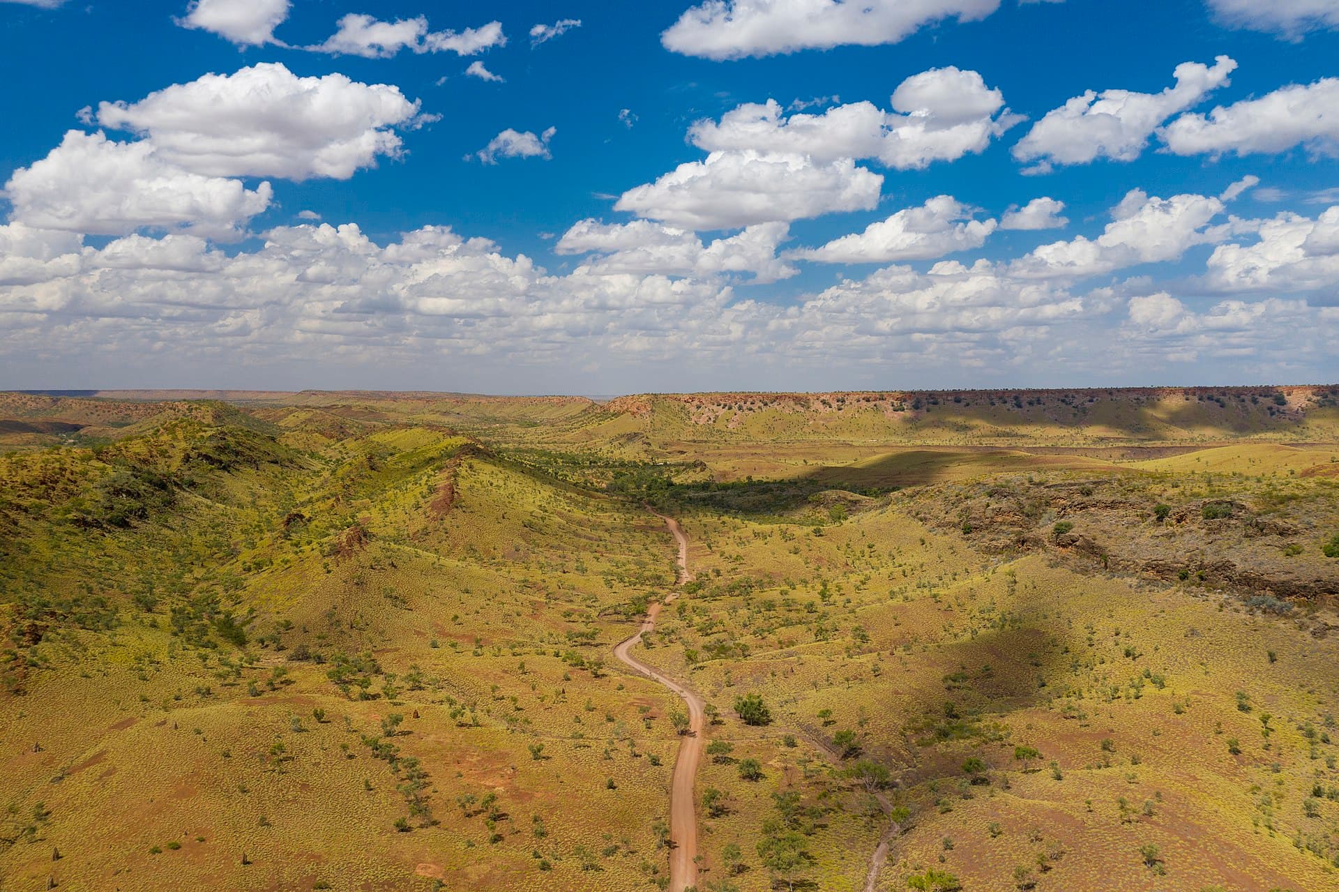 A dirt access track winding through green outback ranges.